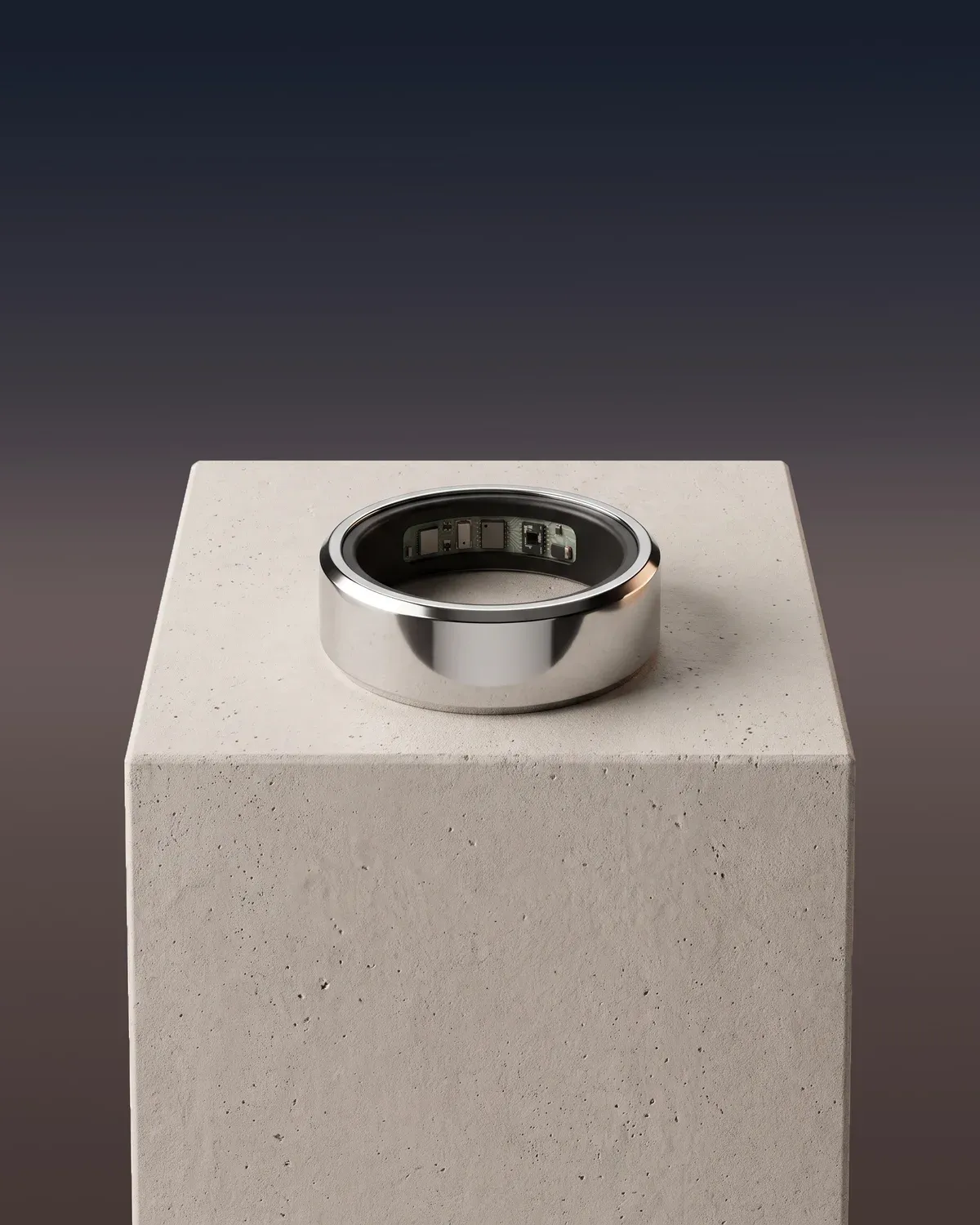The Ain ring in polished silver lying on a stone plinth, its sensors showing inside, against a dusk sky