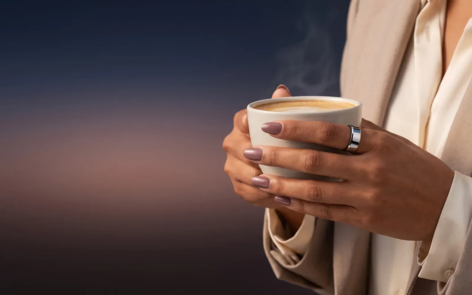 Two hands around a steaming white cup, the silver Ain ring on one finger, a cream jacket against the dawn sky