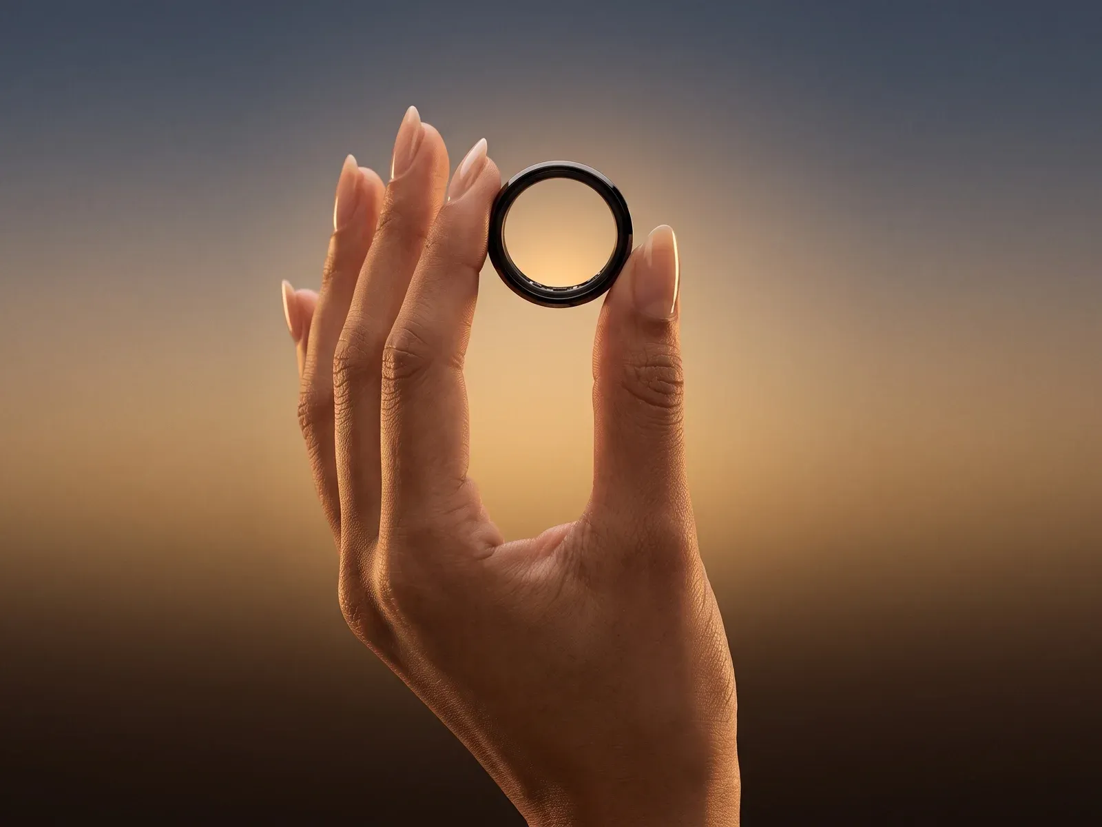 A hand holding the black Hasa ring up to the evening sky between finger and thumb