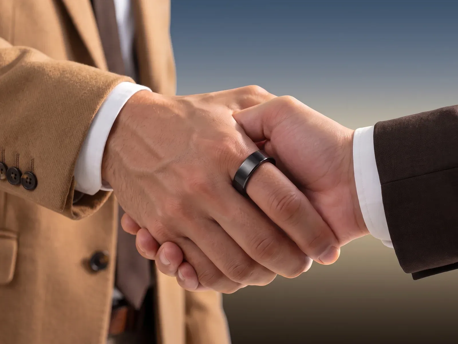 A handshake between two men in suits, the black Hasa ring on one hand
