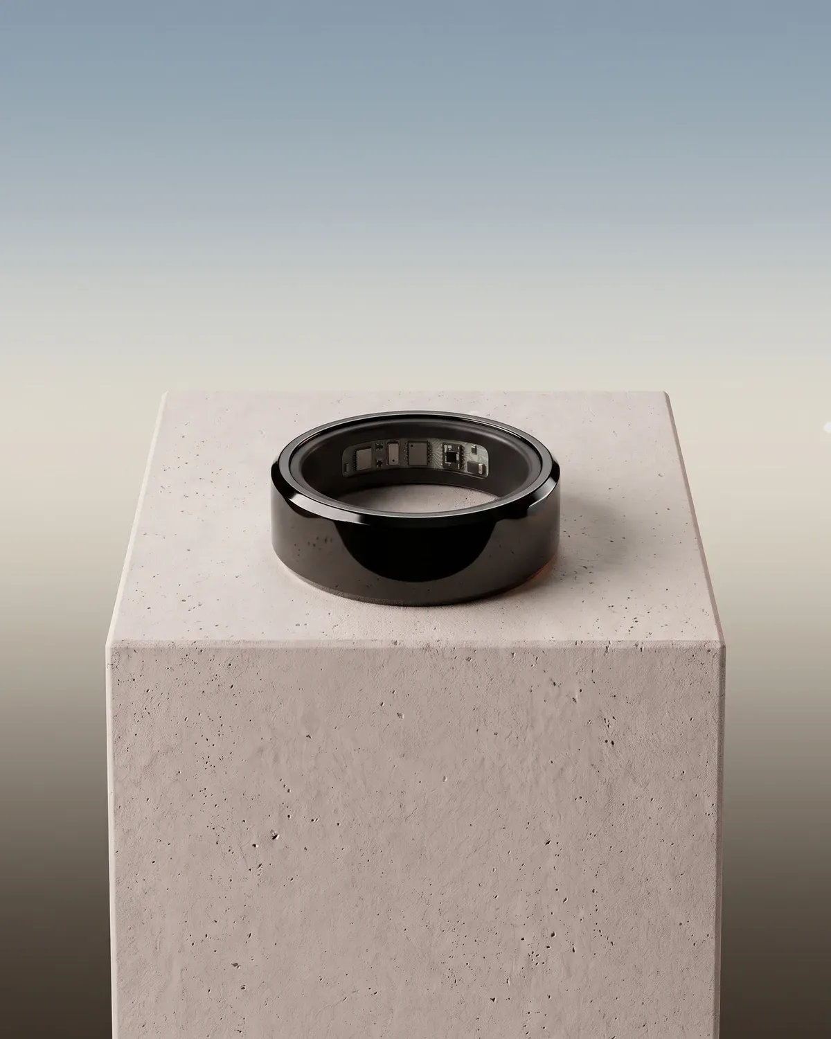 The Hasa ring in glossy black lying on a stone plinth, its sensors showing inside, against a pale morning sky