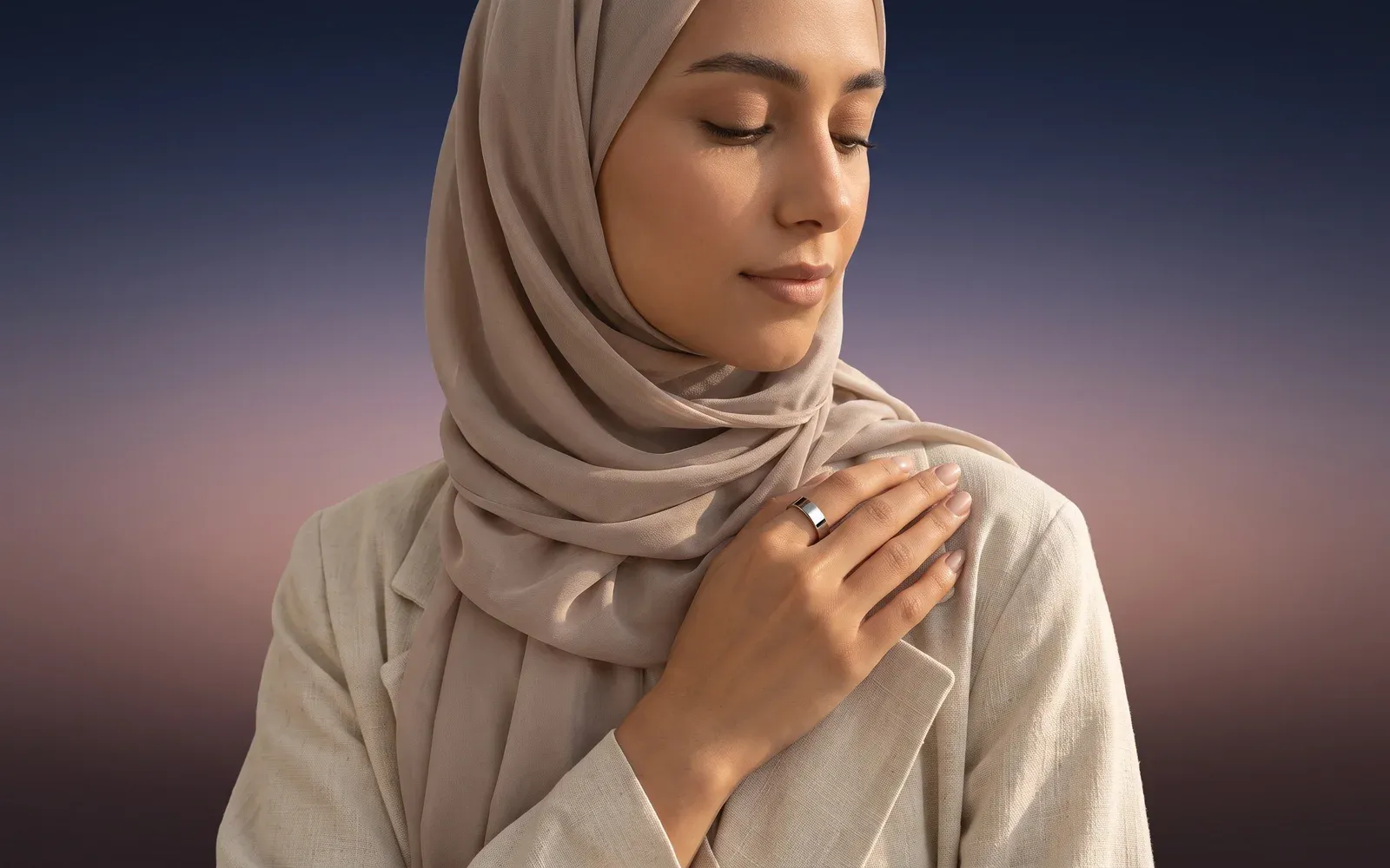 A woman in a hijab with her hand on her chest, a silver ring on her finger