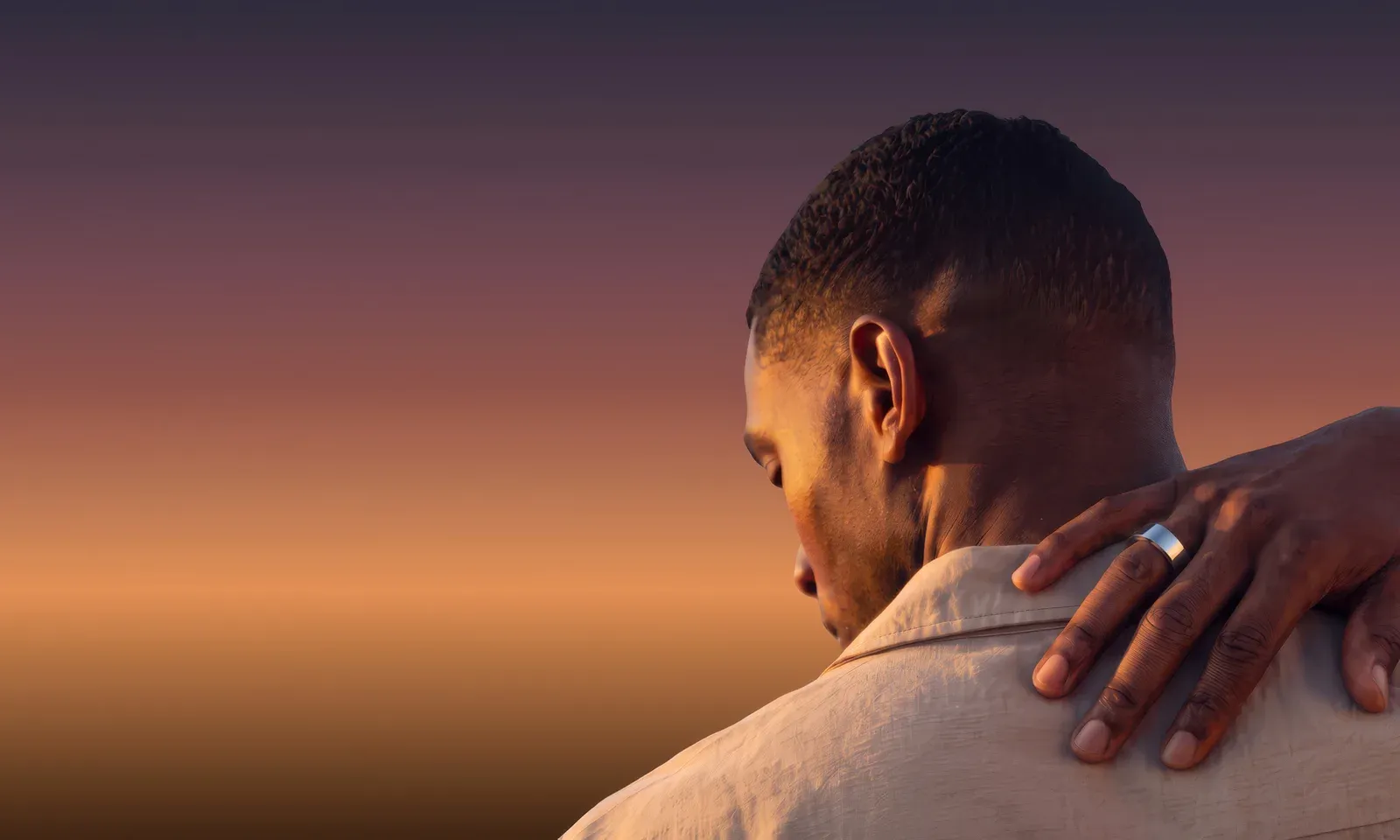 A man seen from behind at sunset, a hand wearing the silver Ain ring resting on his shoulder