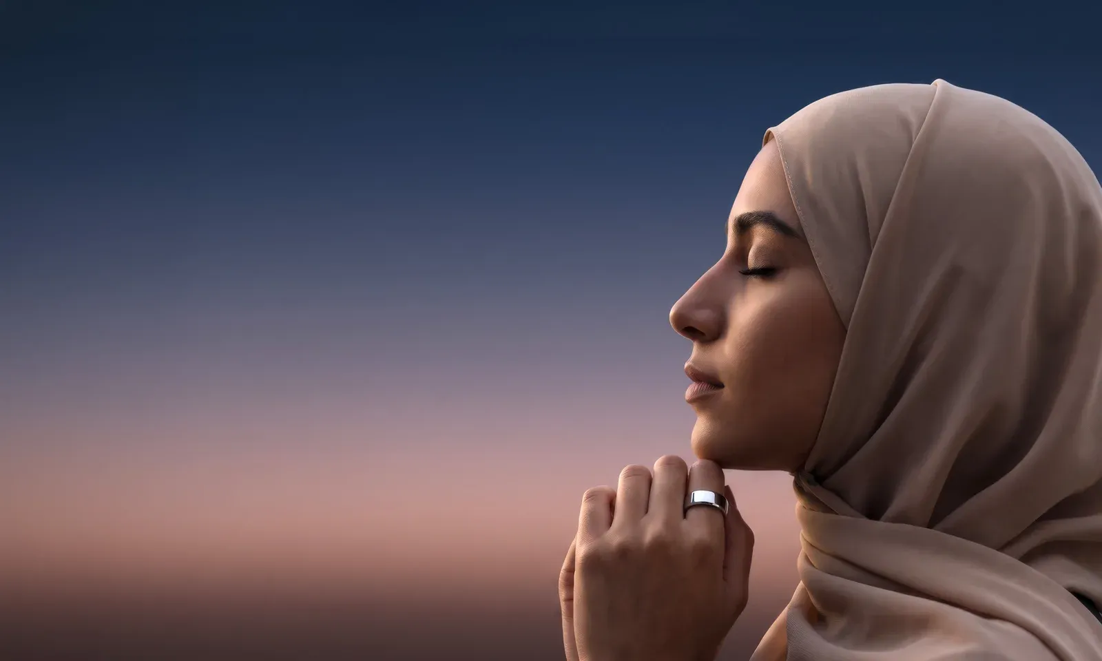 A woman in a sand-coloured hijab with her eyes closed, her hand at her chin wearing the silver Ain ring