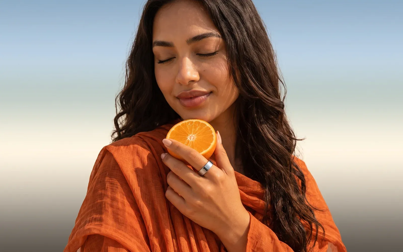 A woman holding half an orange, a silver ring on her finger, an orange scarf around her shoulders