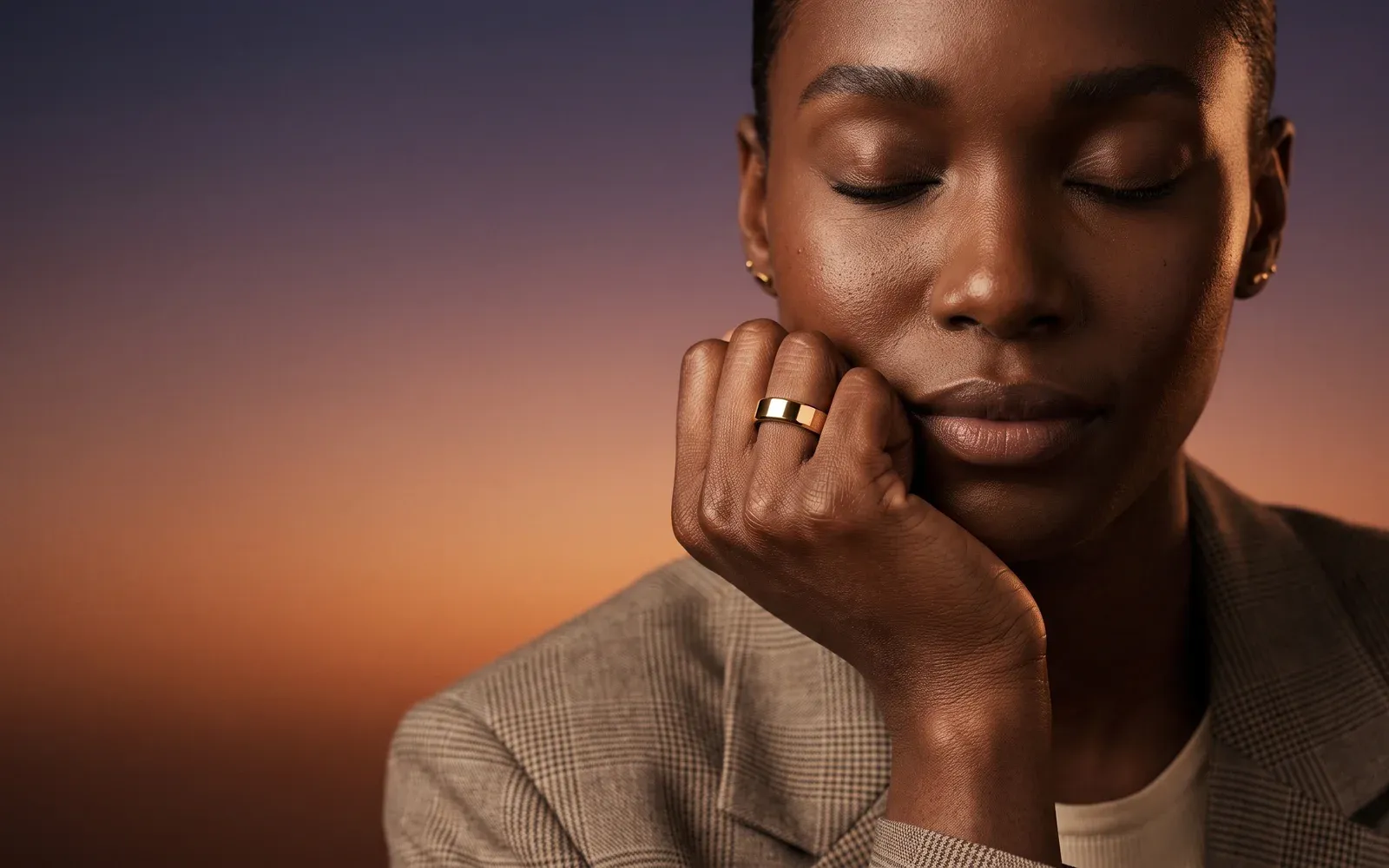 A woman with her eyes closed, her cheek resting on her hand, the gold Liwa ring on her finger