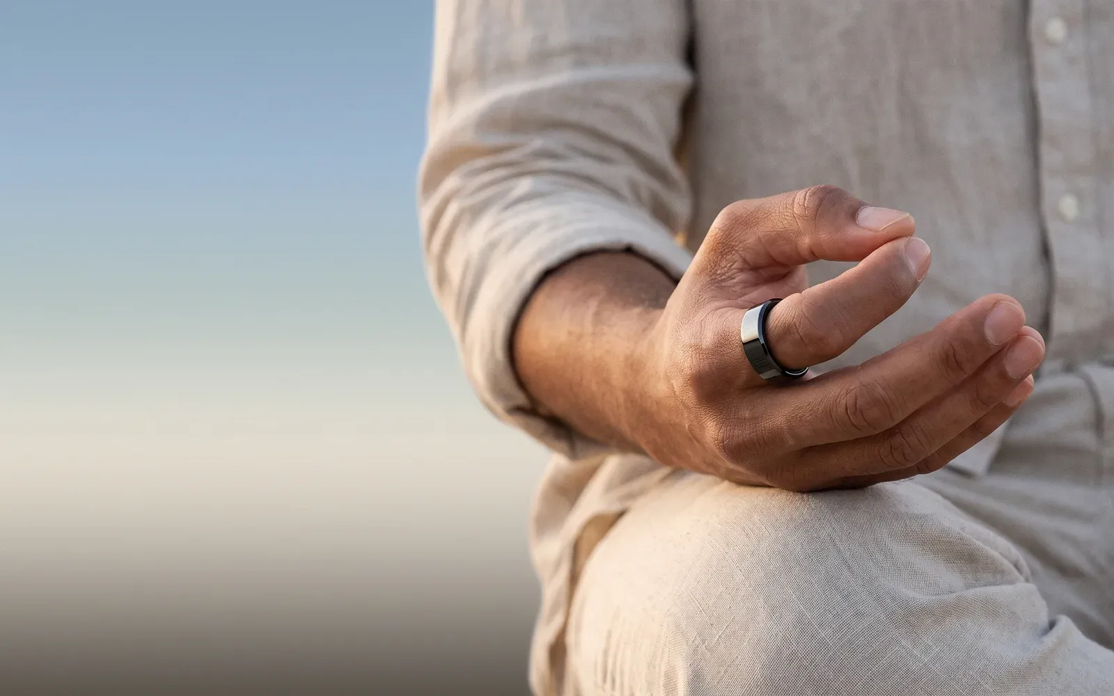 A man in linen sitting at rest, his hand loose on his knee, the black Hasa ring on his finger